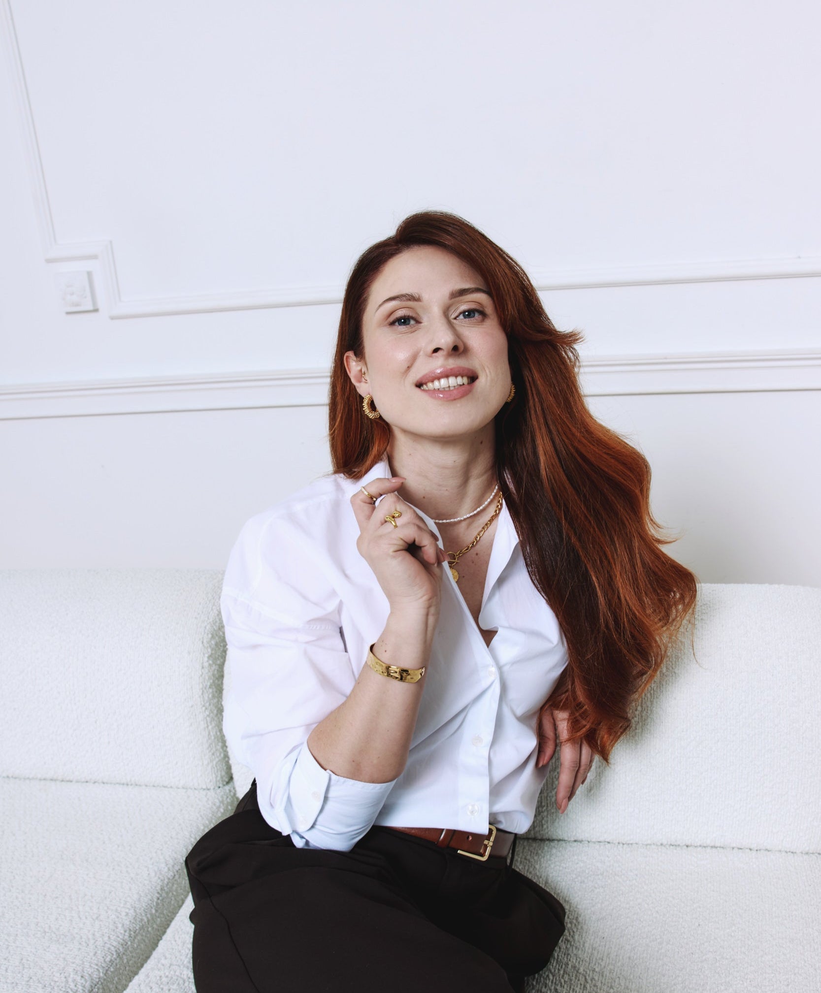 Poshe każdy dzień to twój dzień biżuteria na co dzień modelka siedzi na kanapie trzyma kołnierz uśmiecha się w biżuterii